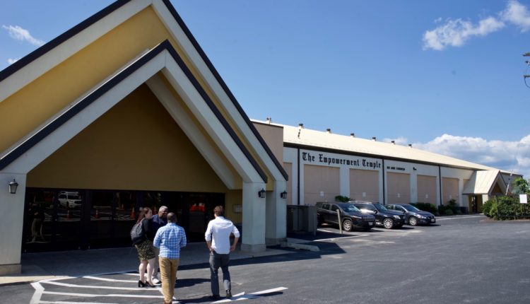 A large angled arch of a building in front of a large parking lot. On the body of the building it reads 